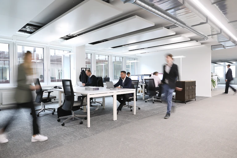 A busy moderne office with glass walls and wooden flooring. The fuzziness of the picture gives an impression of dynamism and movement. 